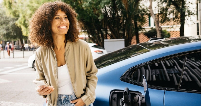 Smiling woman charging her electric car and using her phone